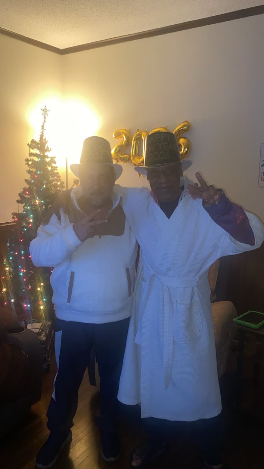 Two residents in robes and party hats posing under 2026 balloons