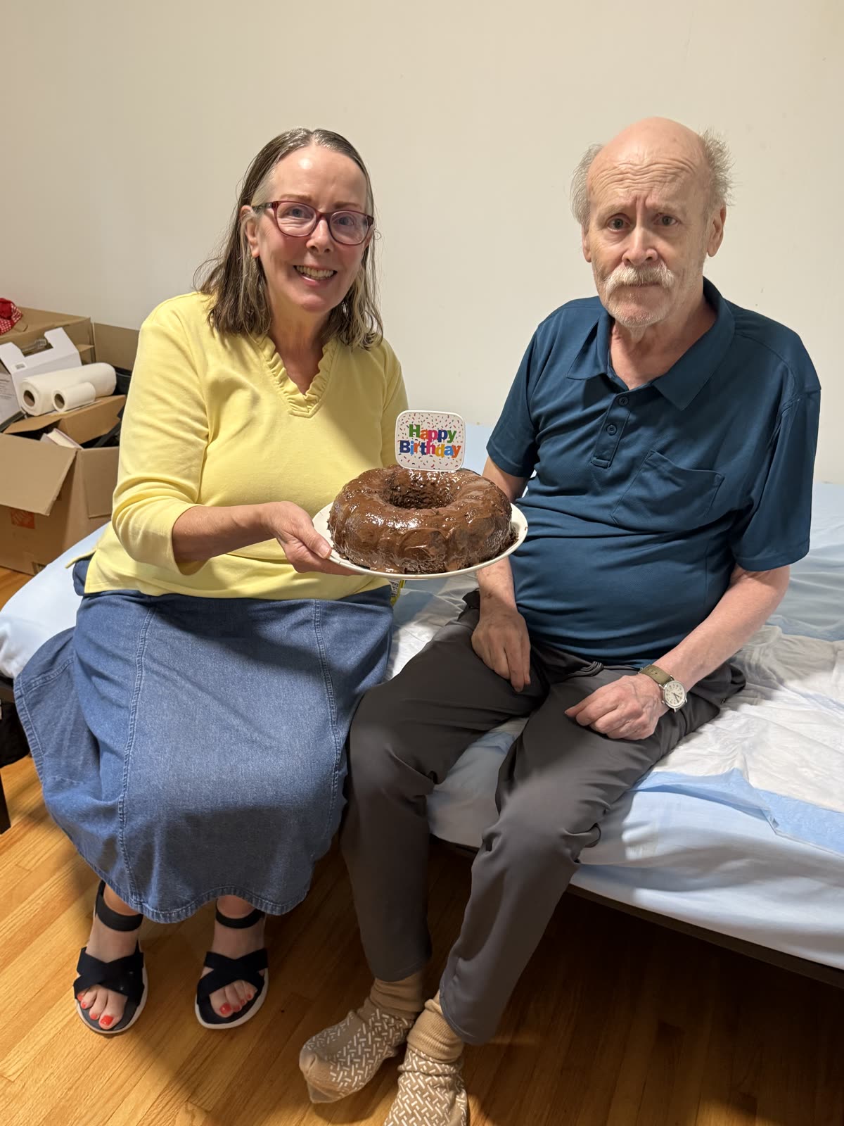 A caregiver presenting a birthday cake to a resident sitting on his bed