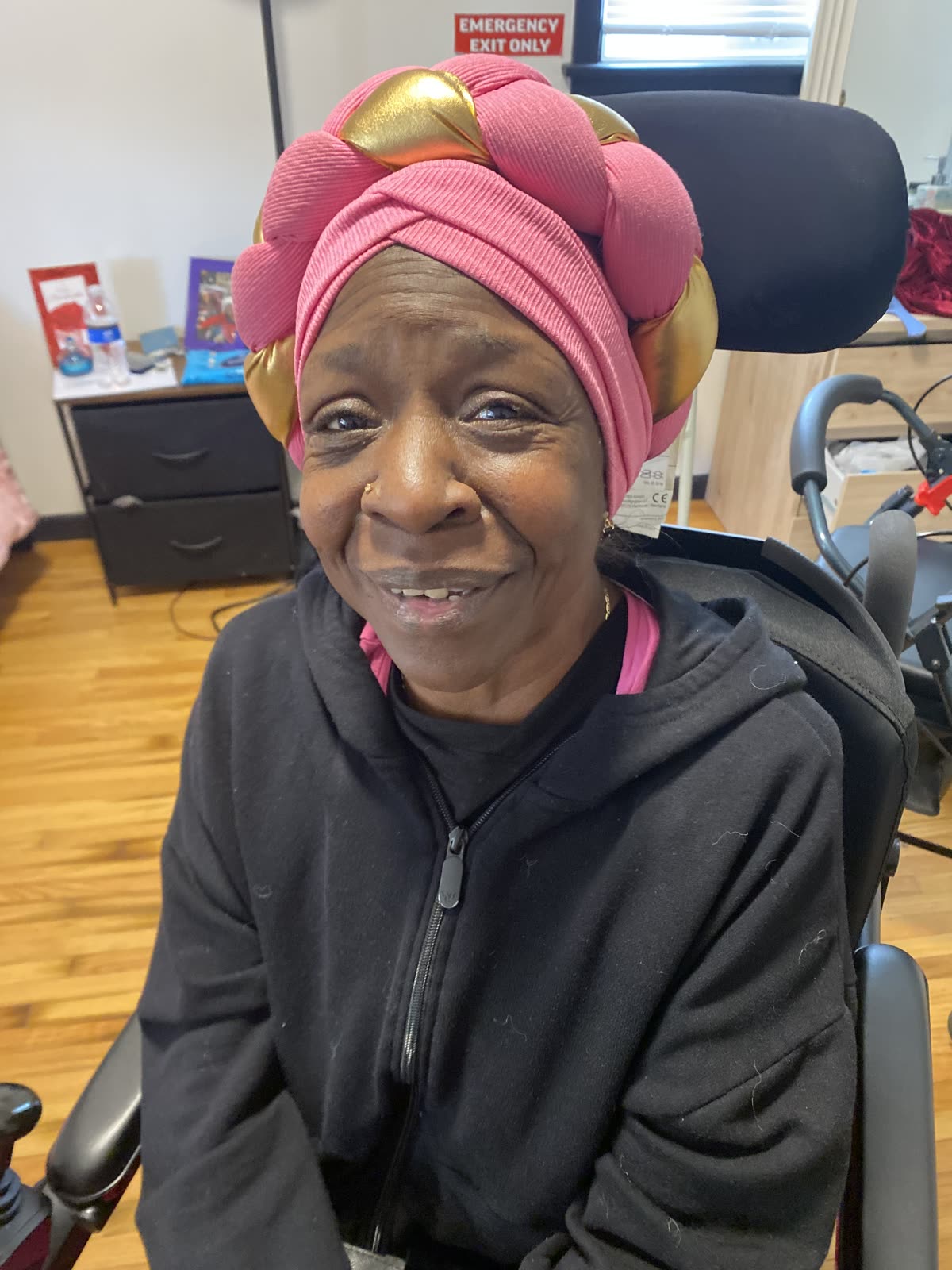 A smiling resident wearing a pink and gold head wrap
