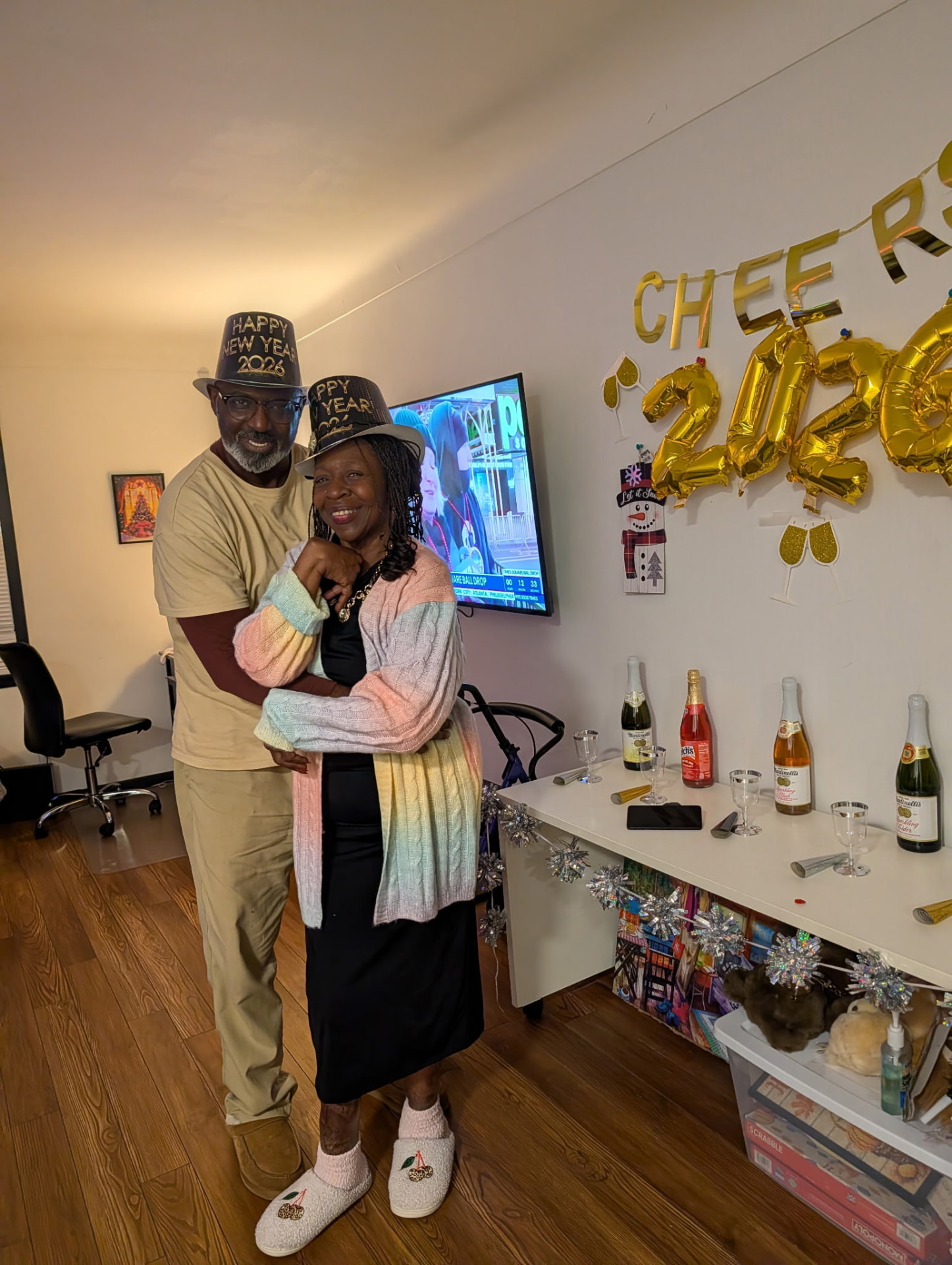 A couple in Happy New Year 2026 hats hugging in the living room