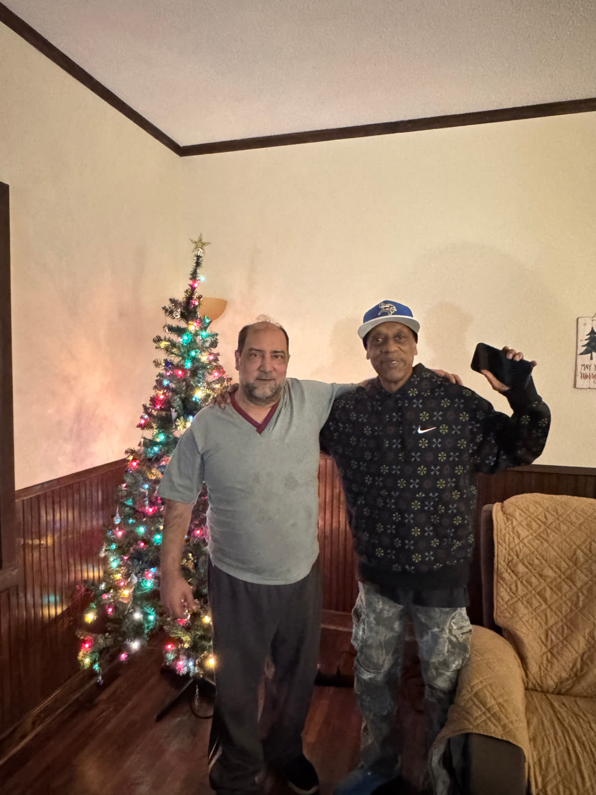 Two residents with arms around each other beside a lit Christmas tree in the living room