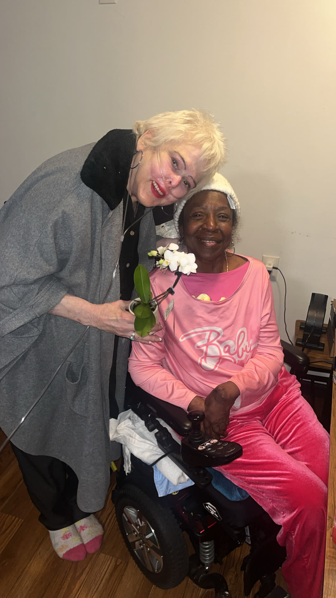 A caregiver leaning in beside a smiling resident who is holding a potted orchid