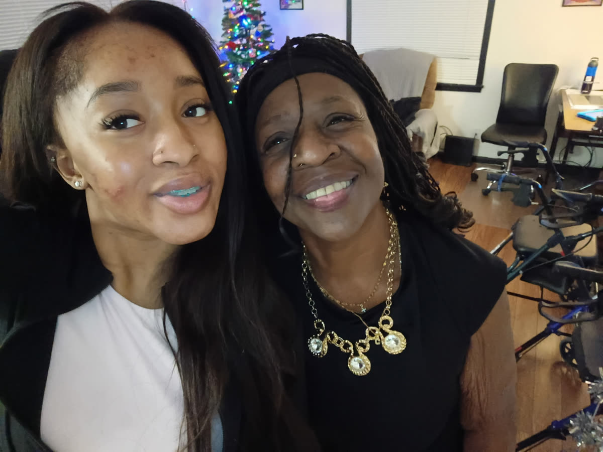 A resident and her granddaughter cheek to cheek, smiling by the Christmas tree